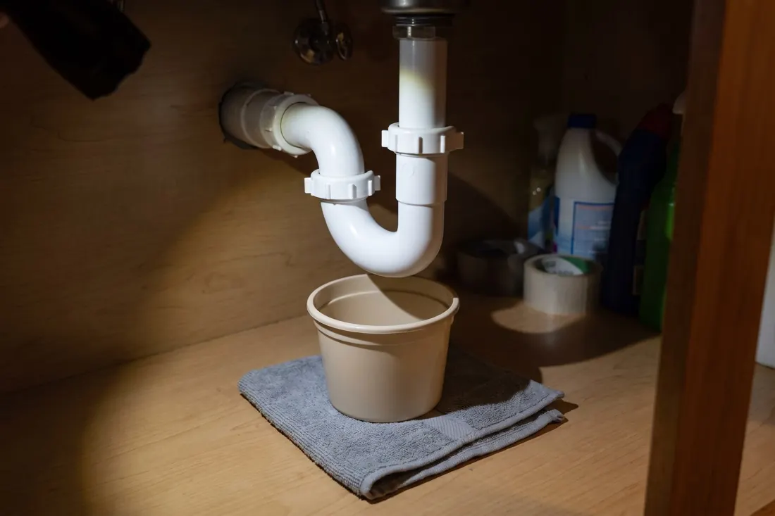 The P-trap under a kitchen sink with a bucket beneath it
