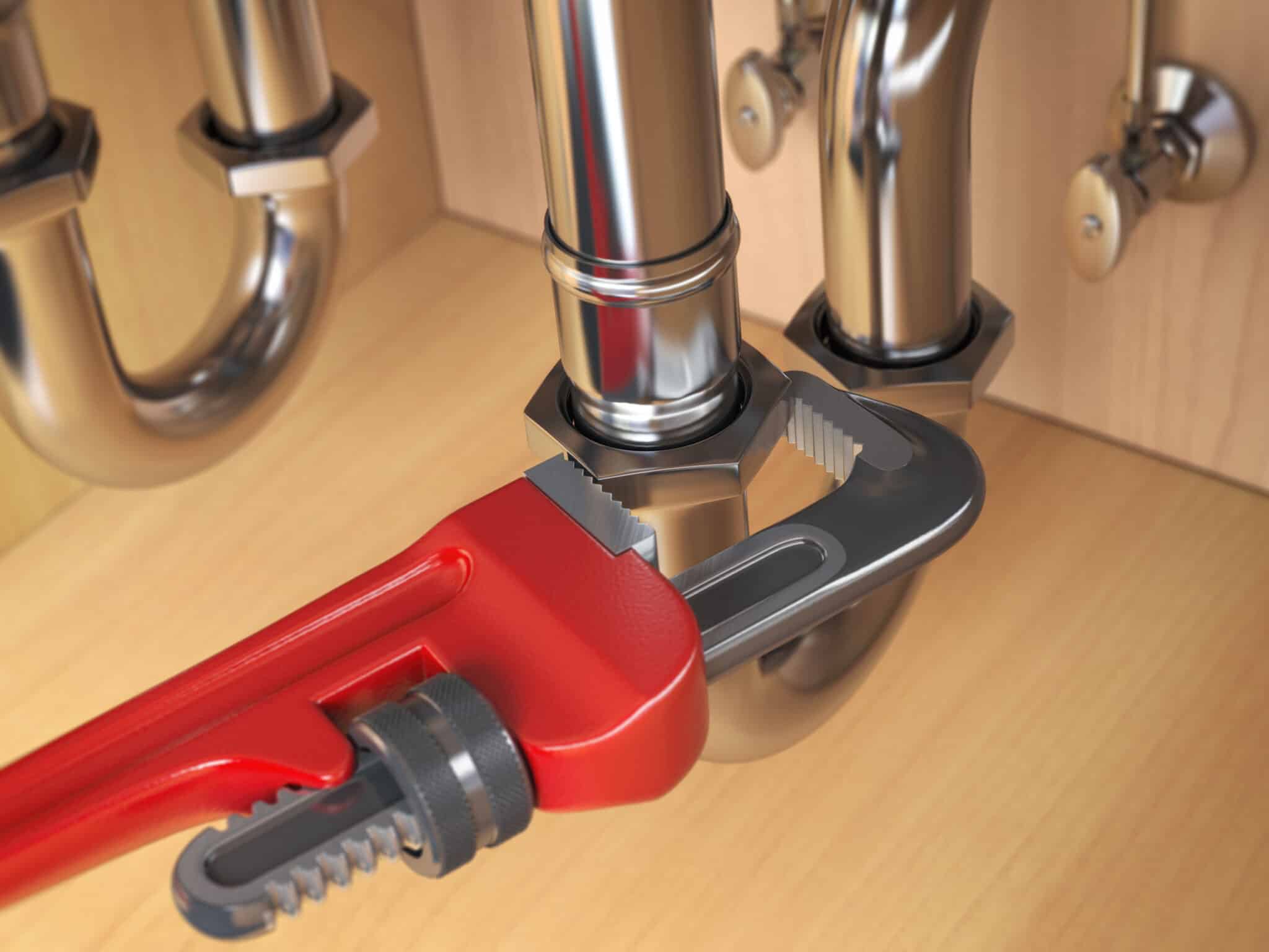 Plumber using an adjustable wrench to repair a water pipe under the sink. Kitchen plumbing issues.